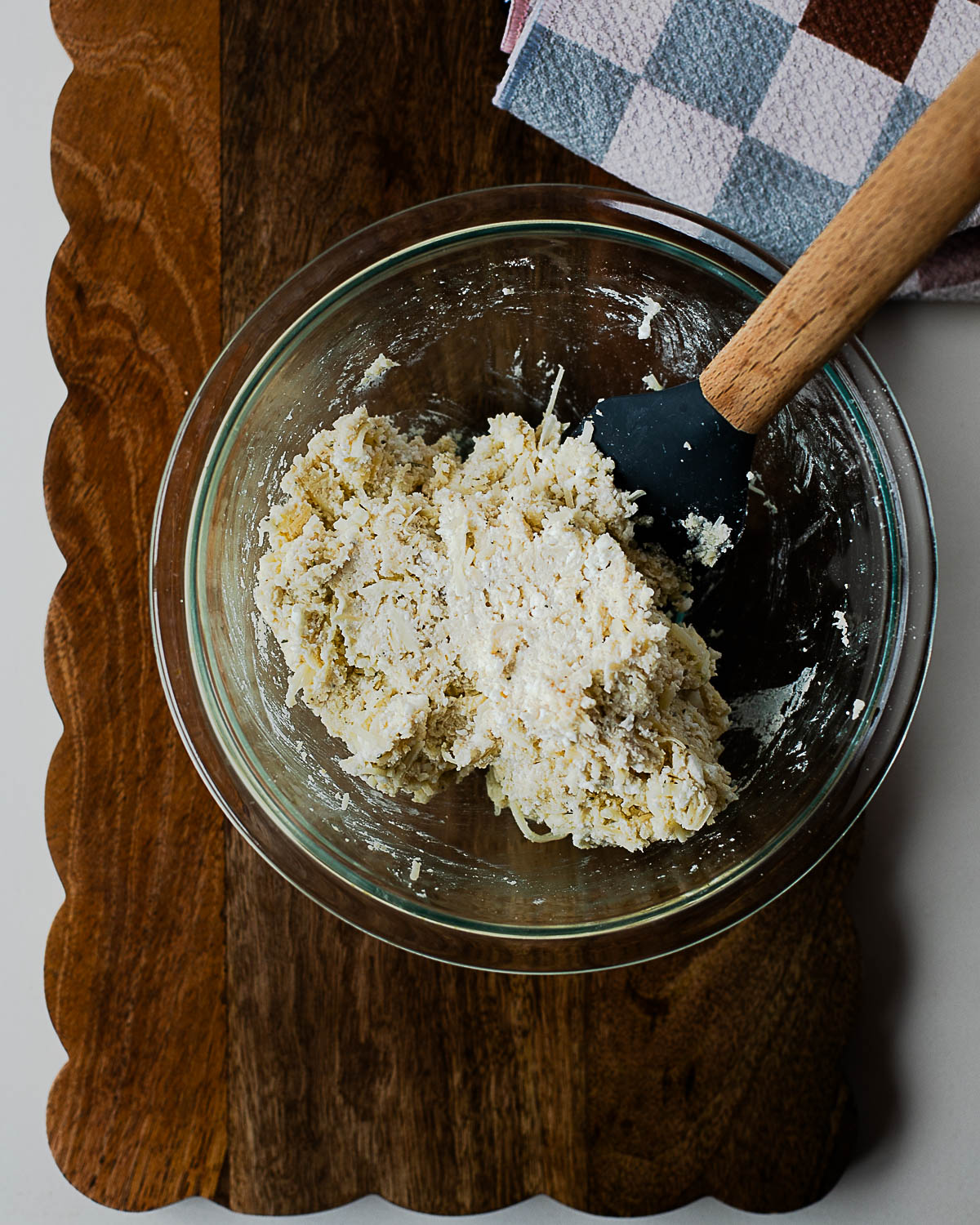 Mixing cottage cheese breadstick dough in a glass bowl with a spatula on a wooden board