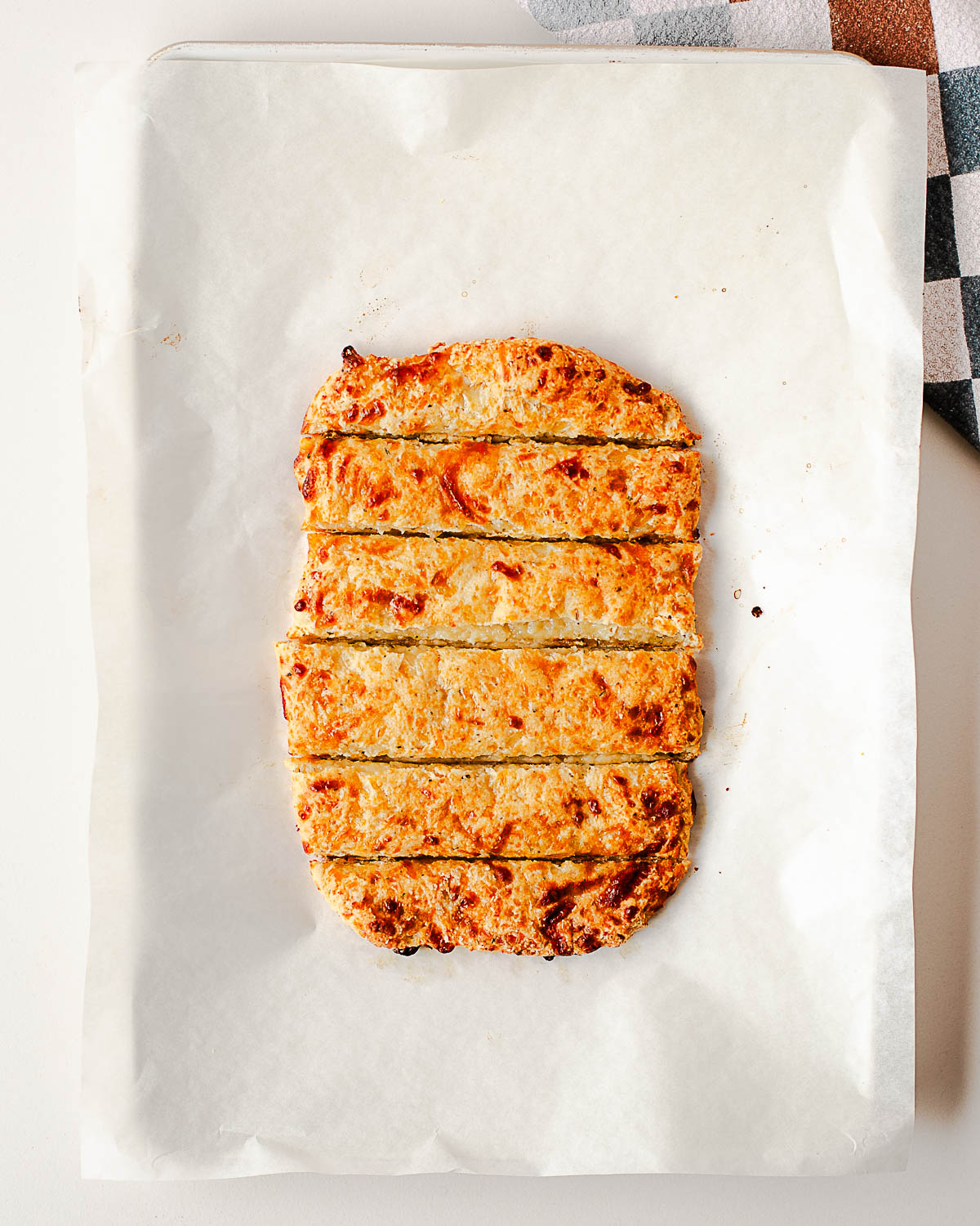 Golden brown baked cottage cheese breadsticks scored into strips on parchment paper