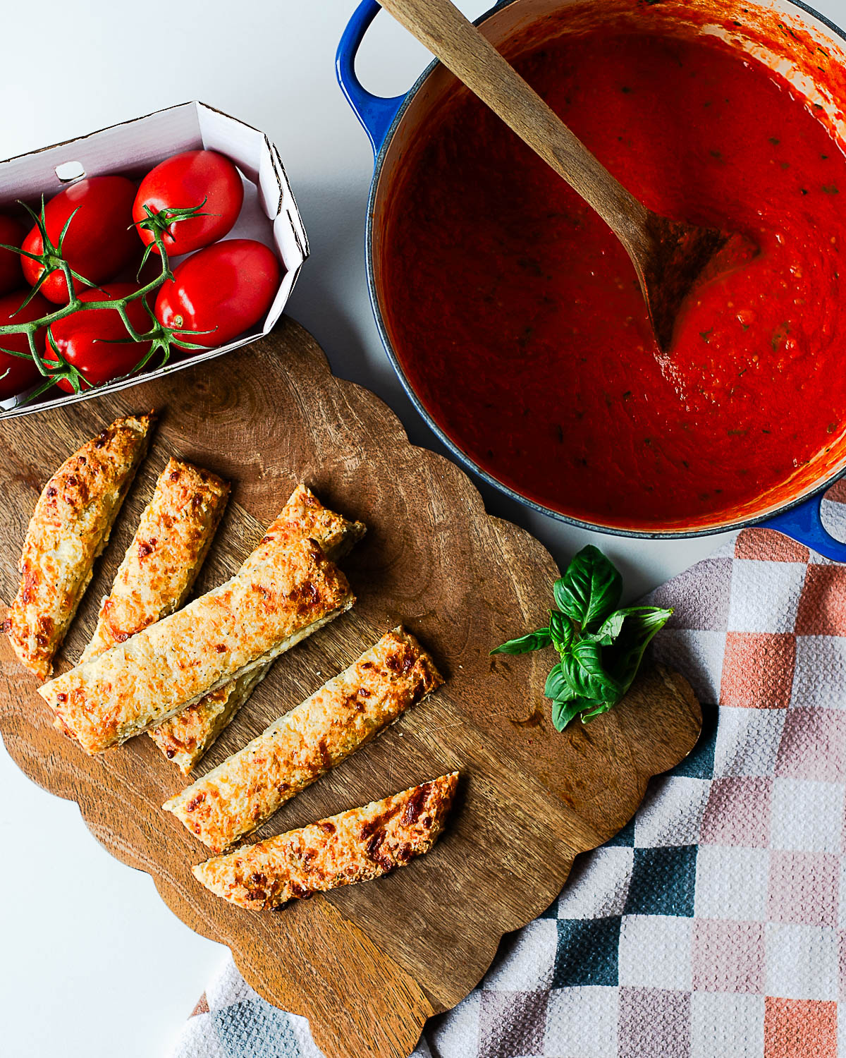 Sliced cottage cheese breadsticks served on a wooden board with a pot of tomato sauce