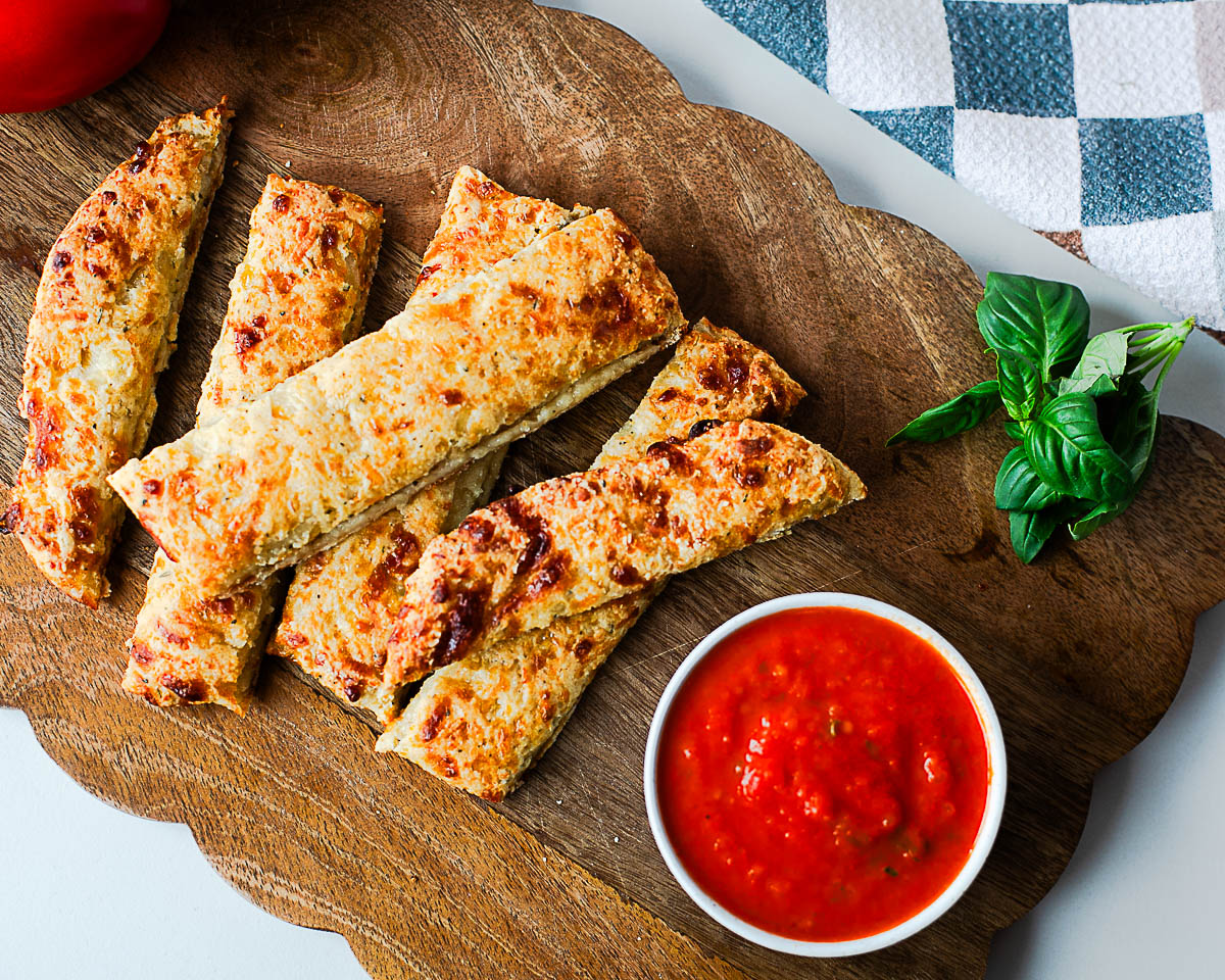 Close-up of golden baked cottage cheese breadsticks stacked on a wooden board