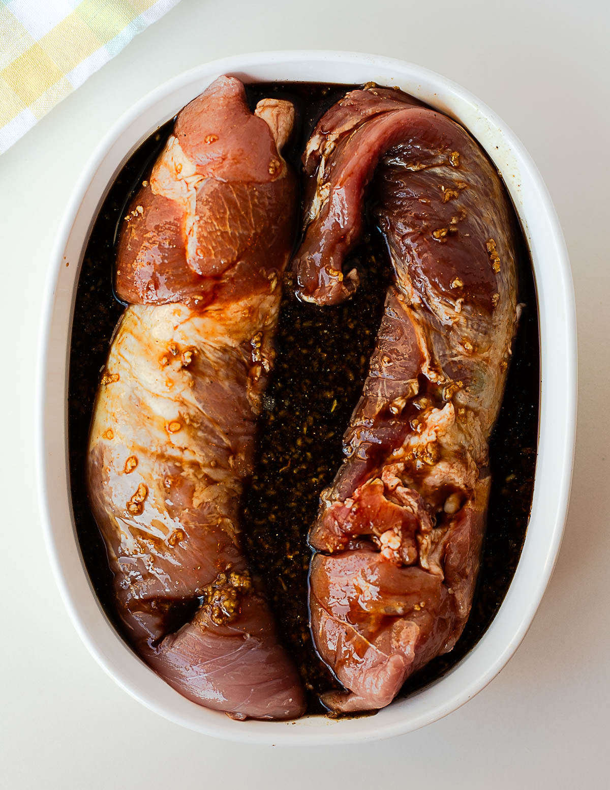 Two pork tenderloins resting in a savory Asian marinade with minced garlic and spices, ready to refrigerate.