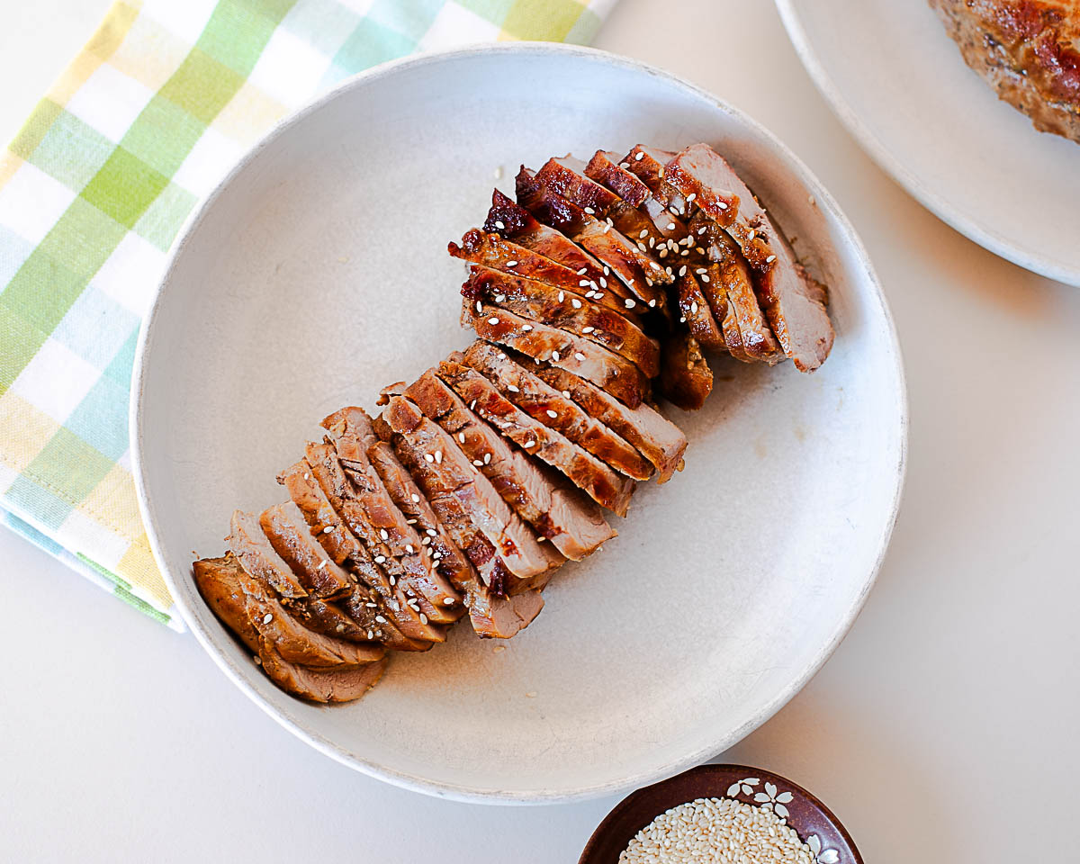 Close-up of juicy, tender slices of Asian pork tenderloin topped with toasted sesame seeds for serving.