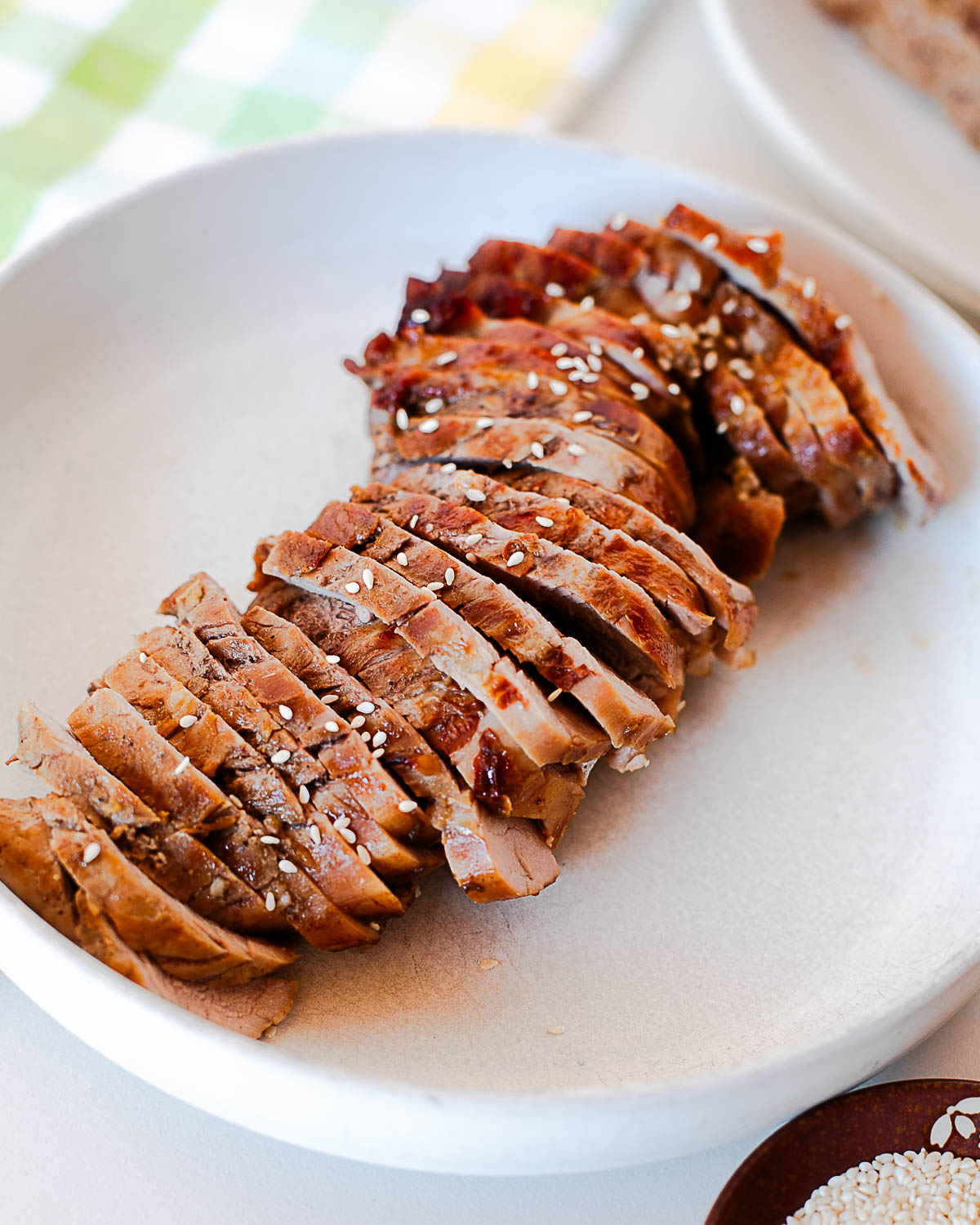 Juicy sliced Asian marinated pork tenderloin arranged on a white plate and sprinkled with sesame seeds.