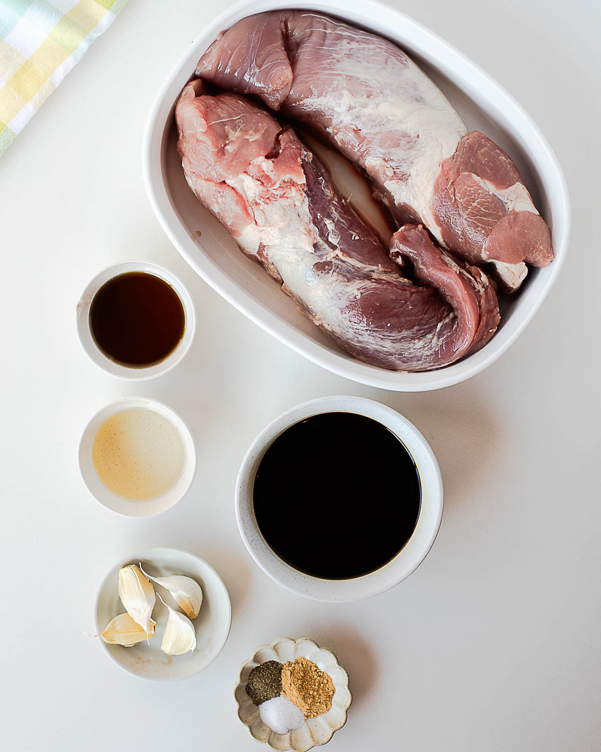 Flat-lay of simple marinade ingredients — pork tenderloin, garlic cloves, coconut aminos, rice vinegar, maple syrup, and spices — on a white surface.