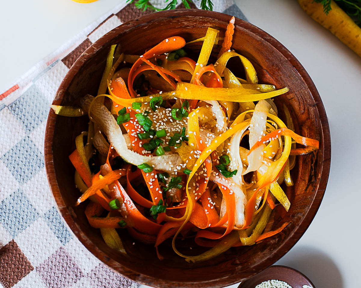 Overhead shot of carrot ribbon salad with sesame seeds and chopped green onions in a wooden bowl