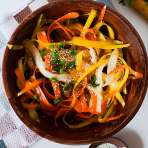 Carrot ribbon salad with orange, yellow, and white ribbons mixed with green onions and sesame seeds, styled on a checkered towel