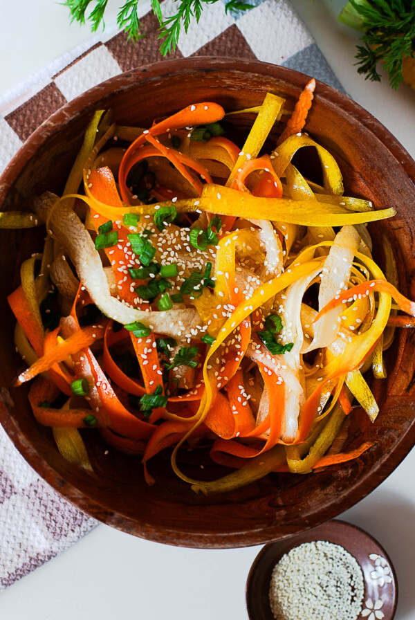 Carrot ribbon salad with orange, yellow, and white ribbons mixed with green onions and sesame seeds, styled on a checkered towel