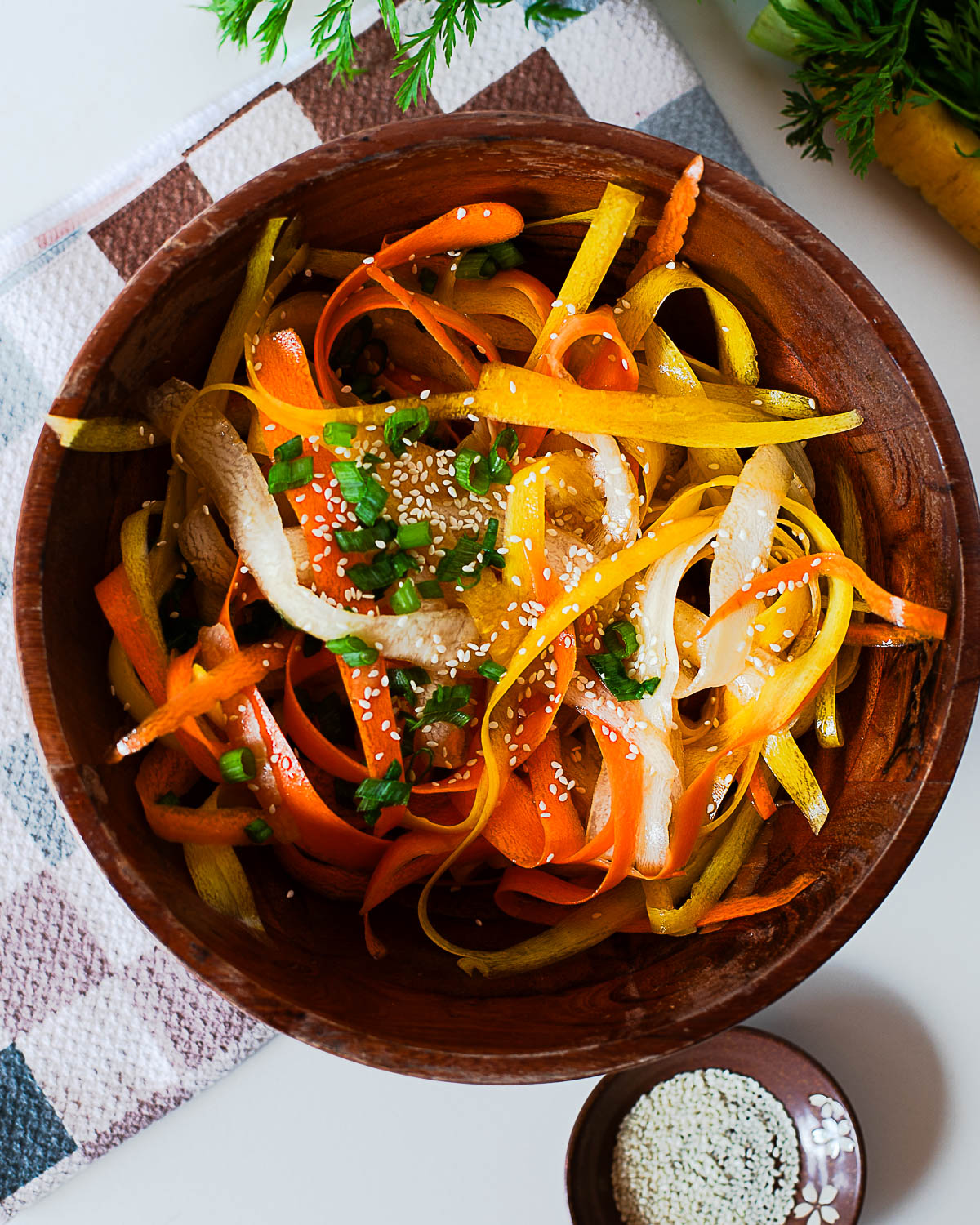 Carrot ribbon salad with orange, yellow, and white ribbons mixed with green onions and sesame seeds, styled on a checkered towel