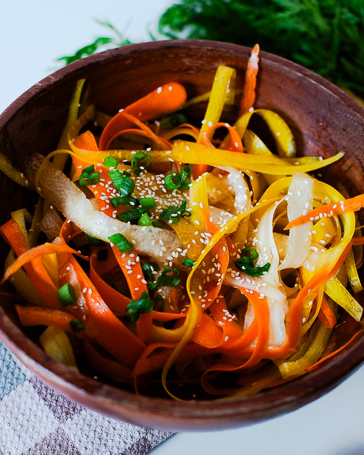 Bright and fresh carrot ribbon salad served in a wooden bowl, garnished with sesame seeds and fresh herbs
