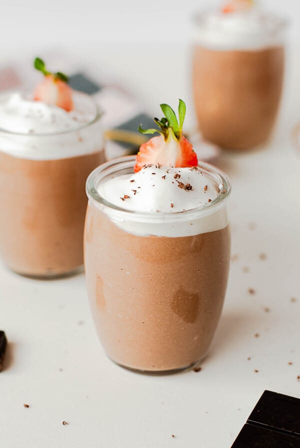 High protein cottage cheese chocolate pudding topped with whipped cream and a fresh strawberry in a glass jar.
