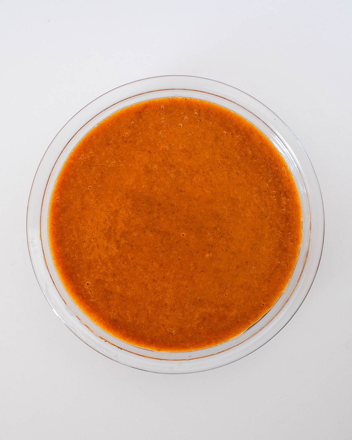 Pumpkin pie filling mixture poured into a glass pie dish, ready to bake — smooth, creamy, and rich in color.