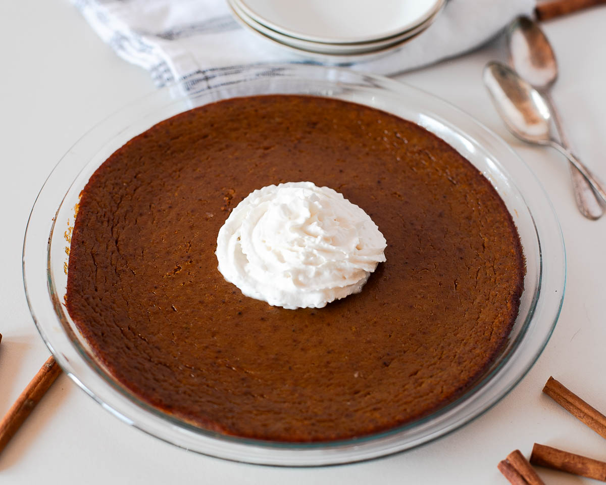 Overhead view of sliced crustless dairy free pumpkin pie served on plates with whipped cream, surrounded by cinnamon sticks for a cozy fall feel.