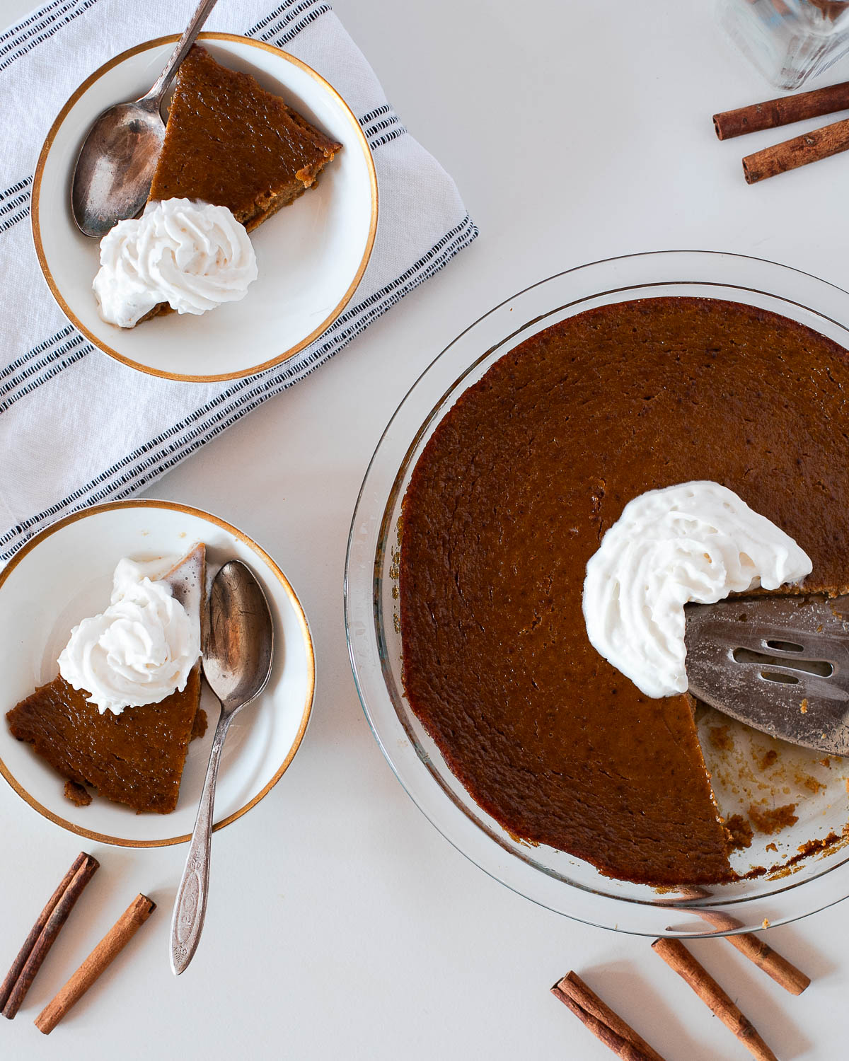 A slice of crustless pumpkin pie being lifted out of the dish with a pie server, showing the silky smooth filling and whipped cream topping.