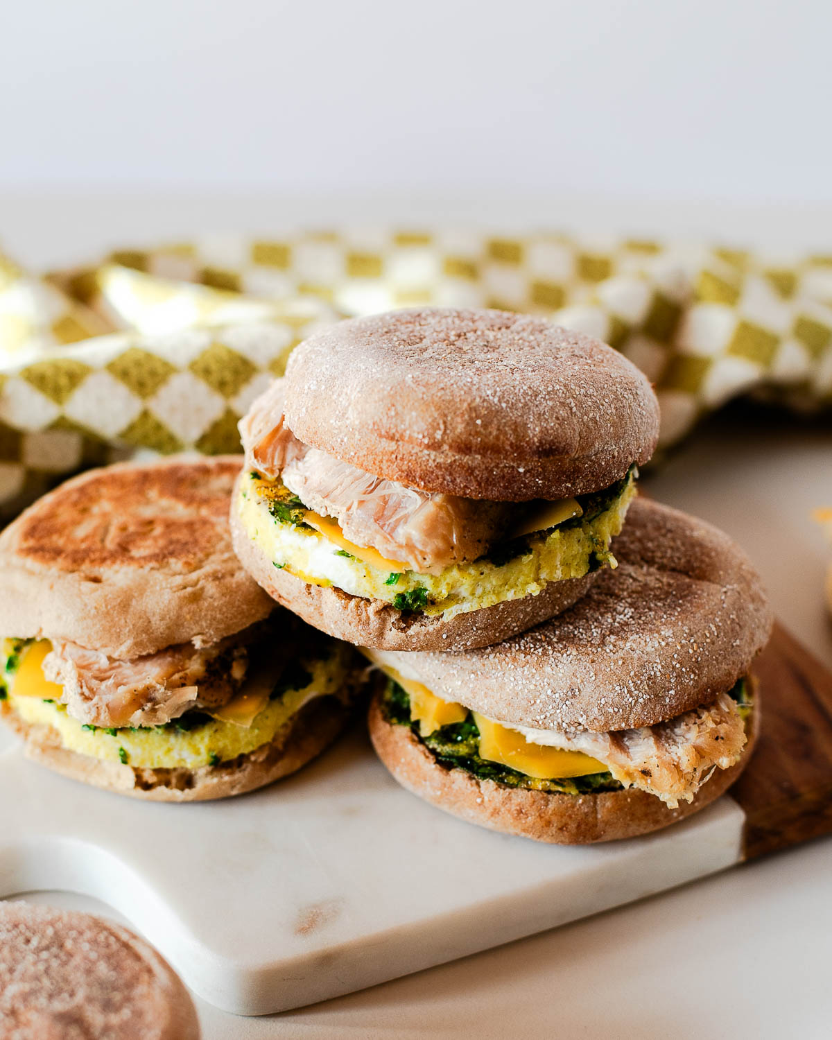 Stacked leftover turkey breakfast sandwiches with cheddar cheese and spinach egg rounds on toasted English muffins.