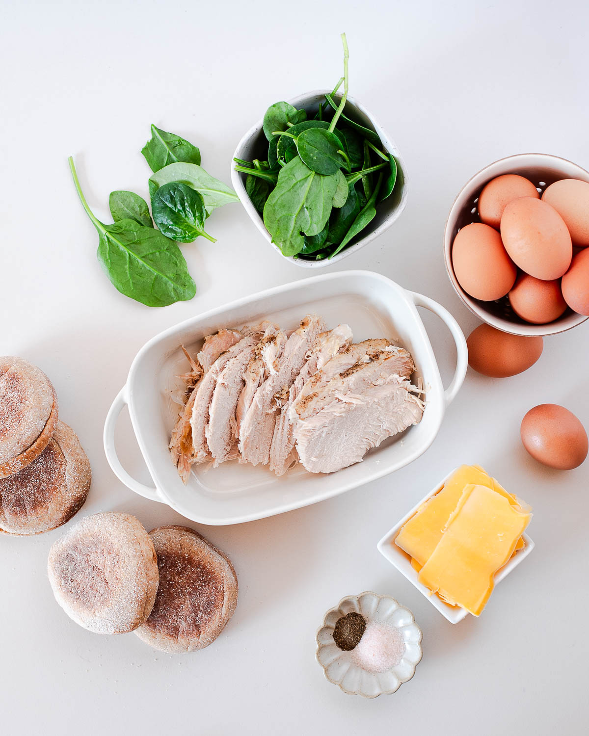 Overhead shot of ingredients for leftover turkey breakfast sandwiches, including eggs, spinach, sliced turkey, cheddar cheese, and English muffins.