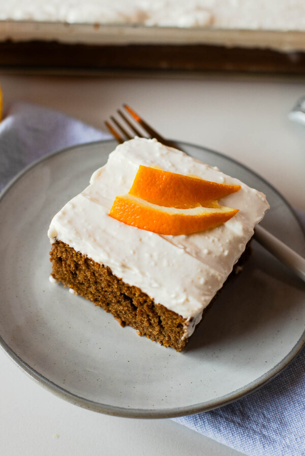 Sweet potato sheet cake slice on a plate with a fork beside it, topped with orange zest ribbons for a bright finish.