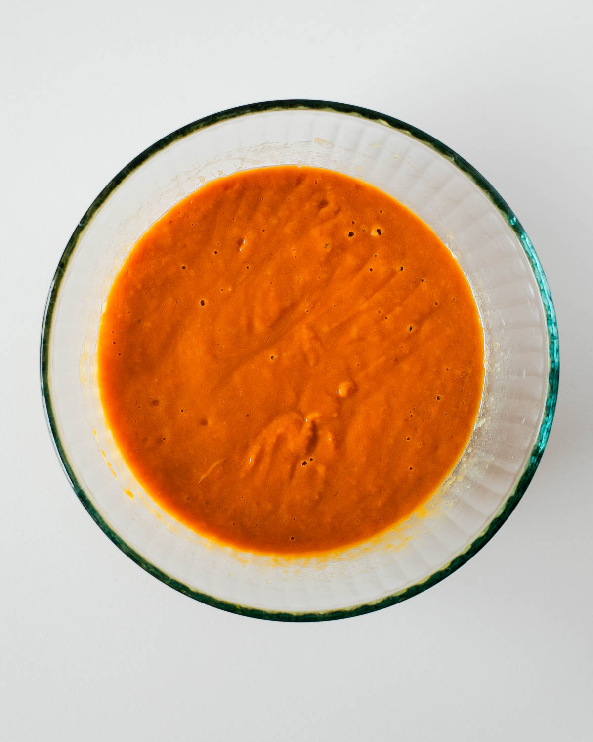 A glass bowl filled with smooth, bright orange sweet potato batter, freshly whisked and ready for the dry ingredients.