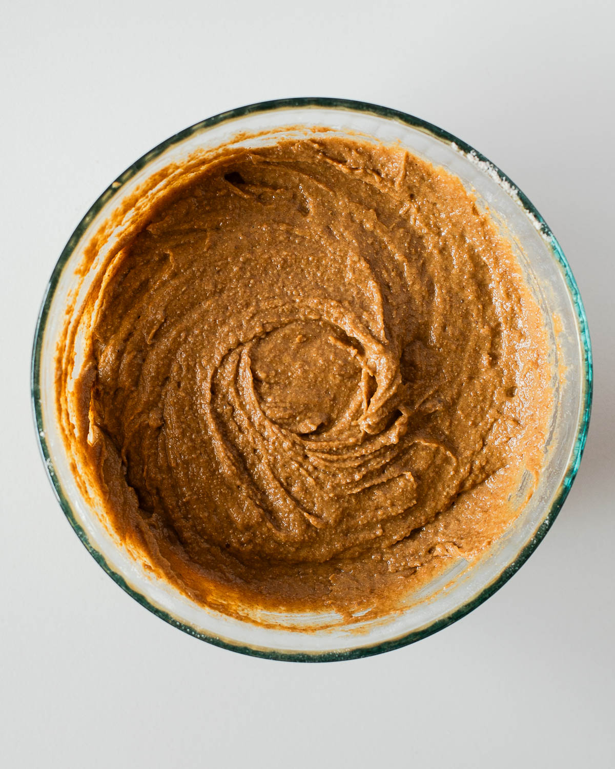 Thick, spiced cake batter in a glass bowl after combining wet and dry ingredients — rich brown color with visible texture from the whole wheat pastry flour.