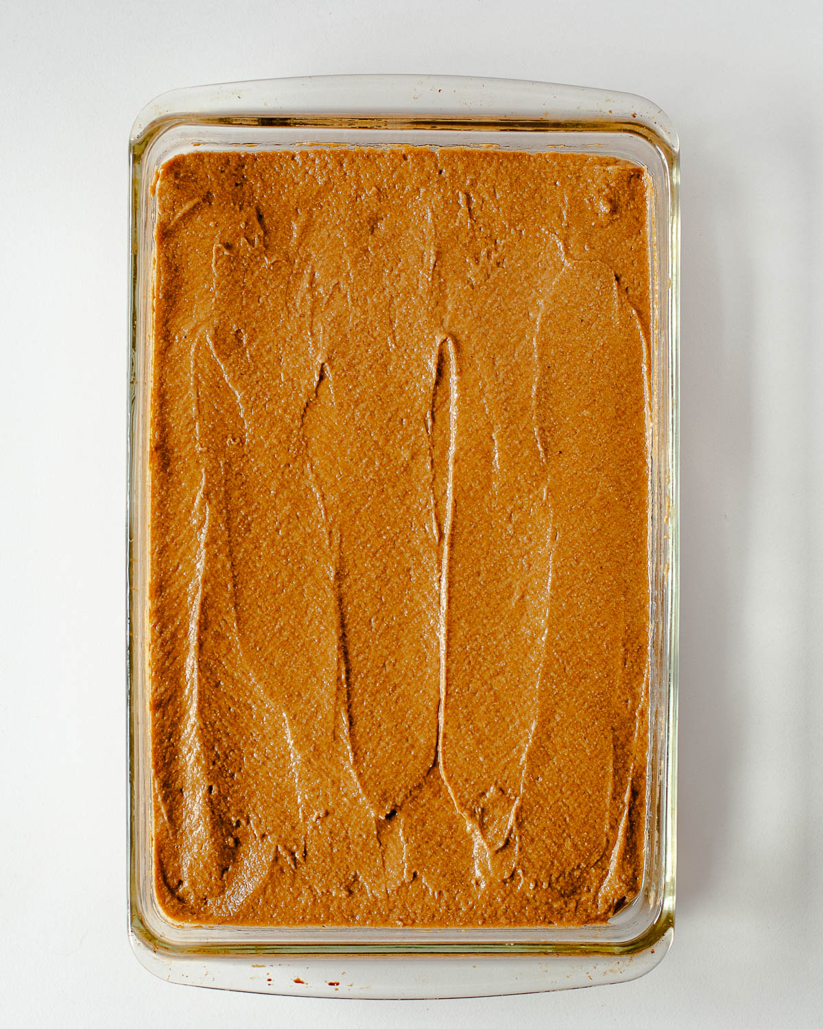 Sweet potato cake batter spread evenly in a greased glass 9x13 baking pan, ready to go into the oven.