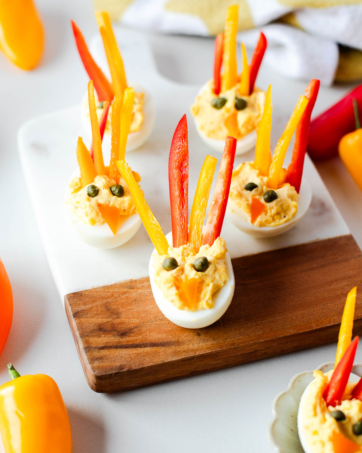 Front view of turkey deviled eggs on a white and wood board, each decorated with bright bell pepper feathers and a tiny orange pepper beak.