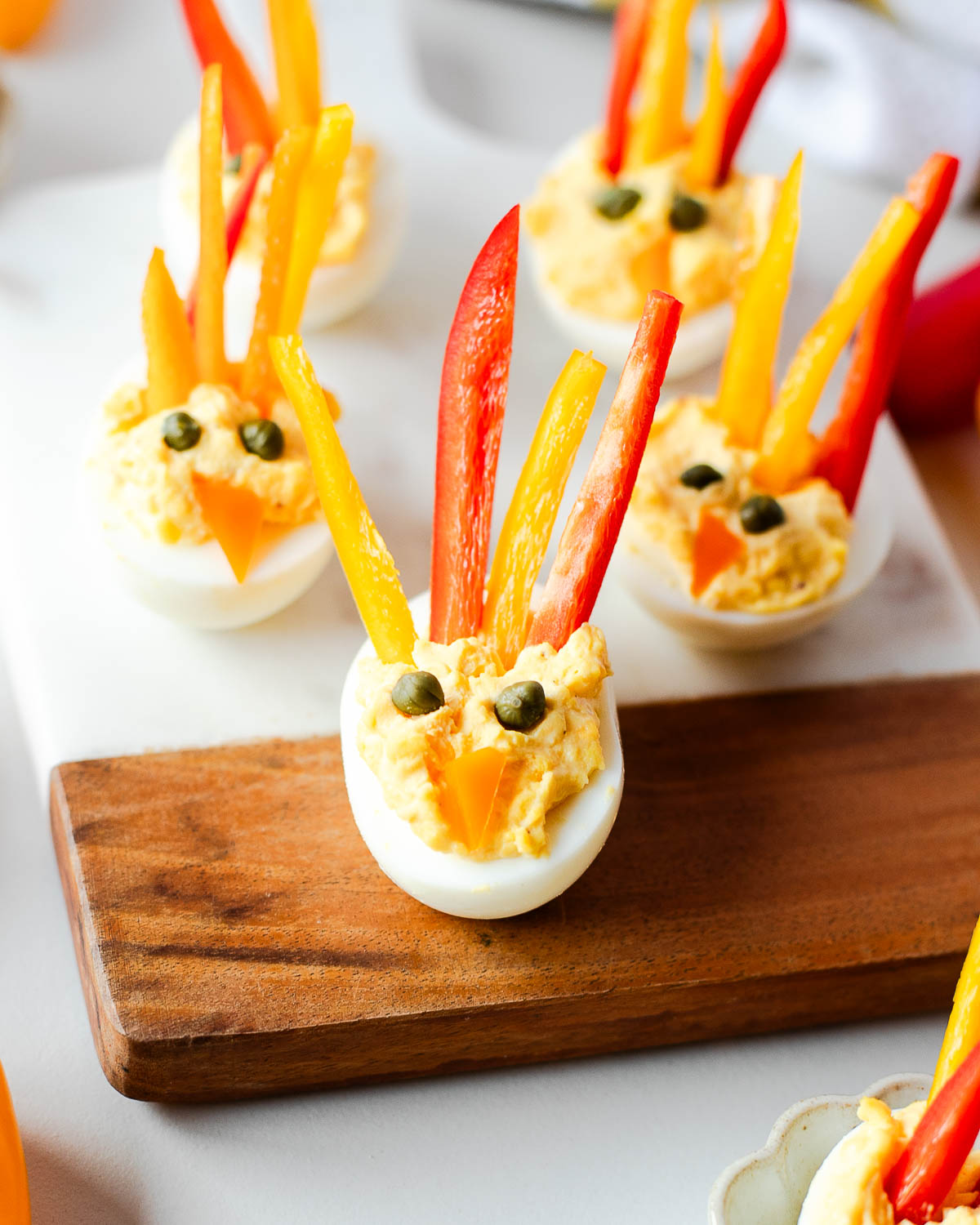 Close-up tray of turkey deviled eggs topped with red and yellow bell pepper strips and capers, displayed with scattered mini peppers on the table.