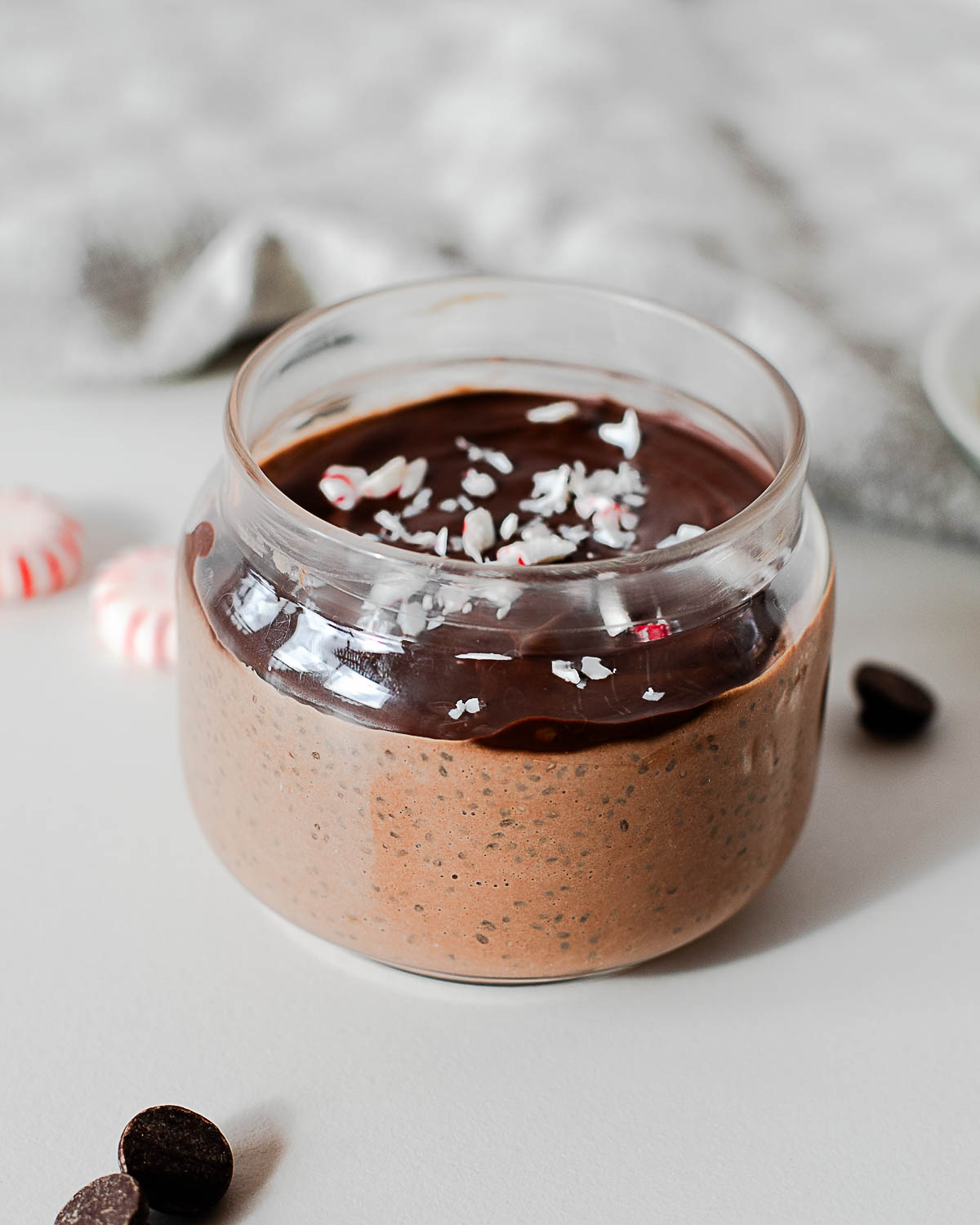 Chocolate peppermint chia pudding in a glass jar with a dark chocolate shell and crushed candy canes