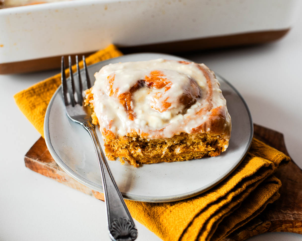 Whole wheat sweet potato pie cinnamon roll topped with cream cheese glaze on a gray plate