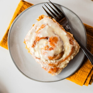 Whole wheat sweet potato cinnamon roll topped with cream cheese glaze on a gray plate