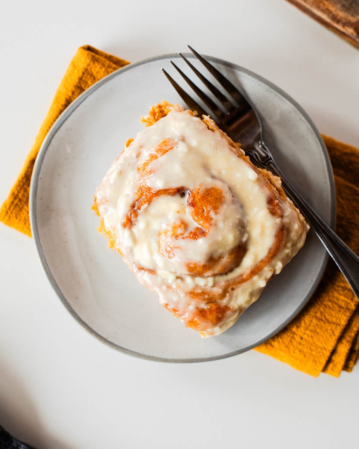 Whole wheat sweet potato cinnamon roll topped with cream cheese glaze on a gray plate