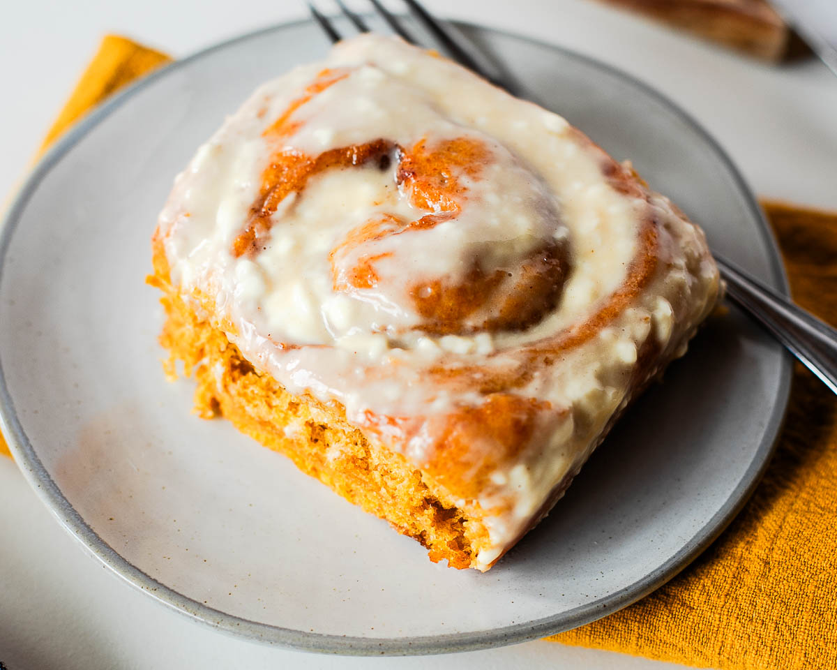 Sweet potato pie cinnamon roll with cream cheese frosting on a plate