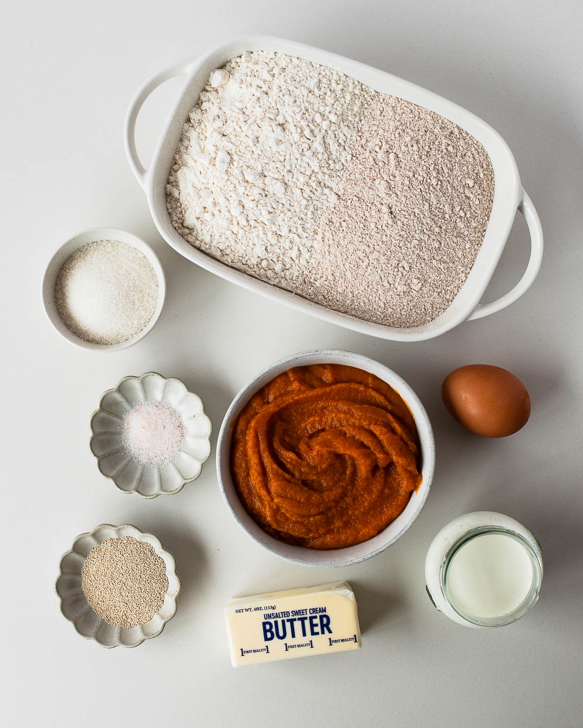 Ingredients for sweet potato pie cinnamon rolls including flour, yeast, sweet potato purée, butter, egg, and milk