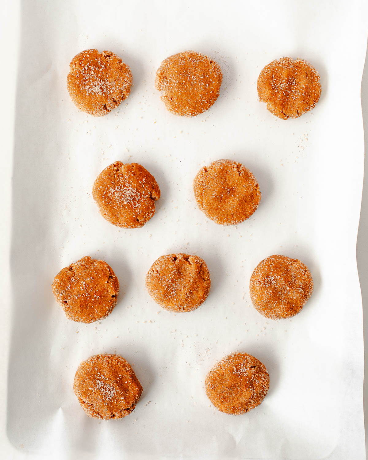 Unbaked sweet potato snickerdoodle cookies rolled in cinnamon sugar and pressed onto a parchment lined baking sheet
