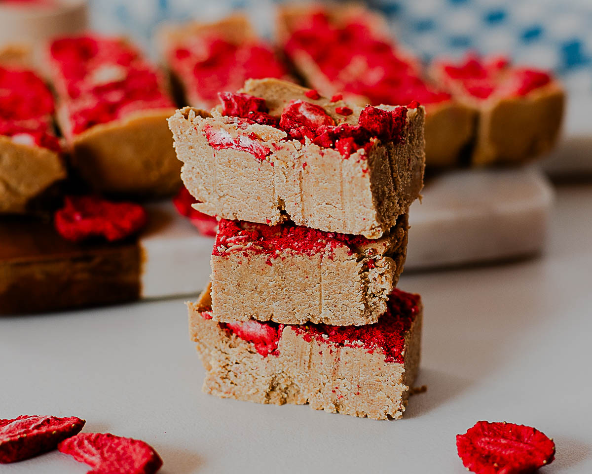 Close-up of three stacked peanut butter protein fudge pieces with bright red freeze-dried strawberry topping.