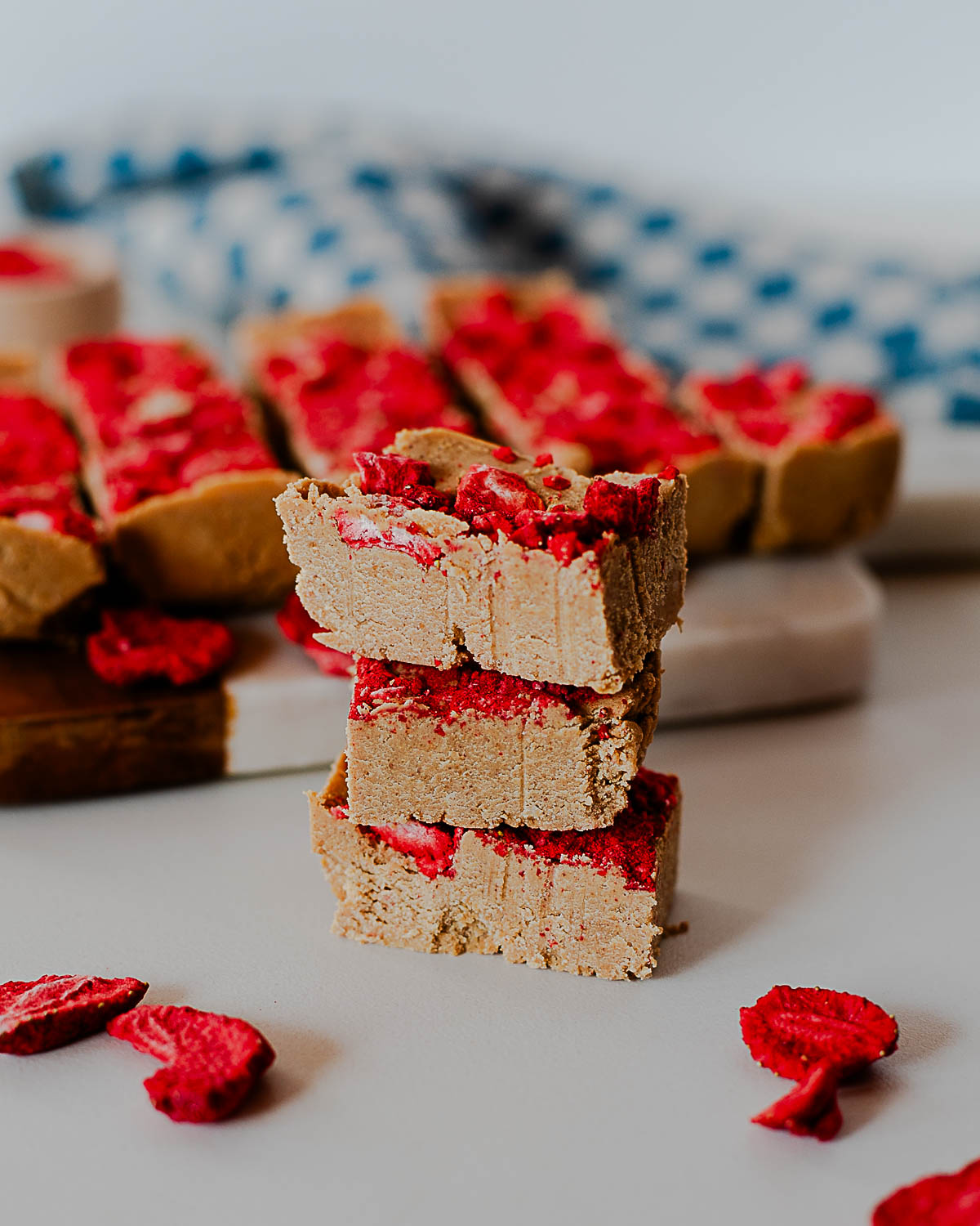 stack of PB&J protein fudge squares on a cutting board with freeze-dried strawberries scattered around.