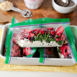 Close-up of a zip-top smoothie pack filled with protein powder, freeze-dried berries, and spinach flakes with more ingredients in the background.