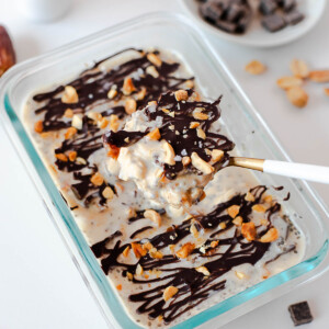 Snickers overnight oats with a spoon lifting a bite of creamy oats, chocolate drizzle, and peanuts