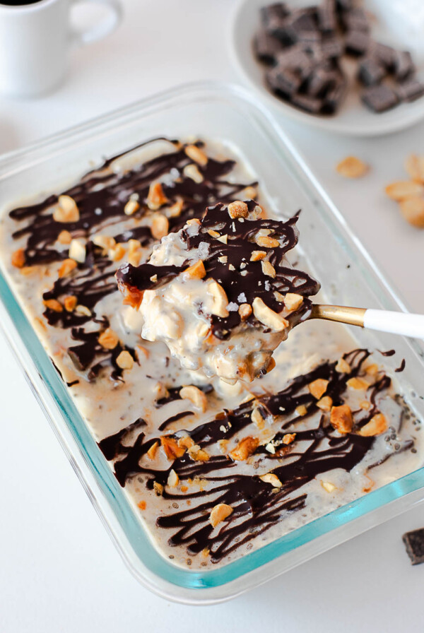 Snickers overnight oats with a spoon lifting a bite of creamy oats, chocolate drizzle, and peanuts