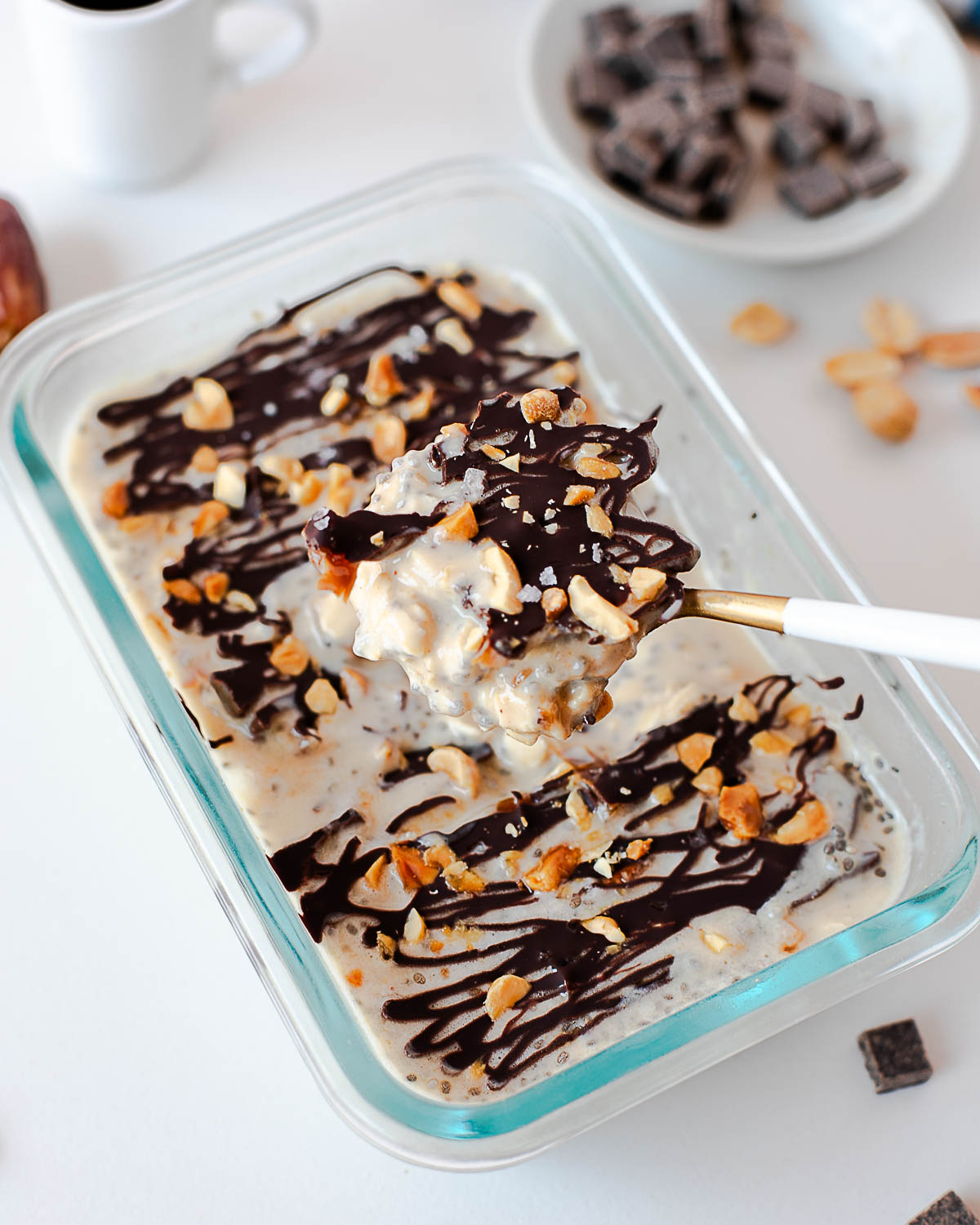 Snickers overnight oats with a spoon lifting a bite of creamy oats, chocolate drizzle, and peanuts