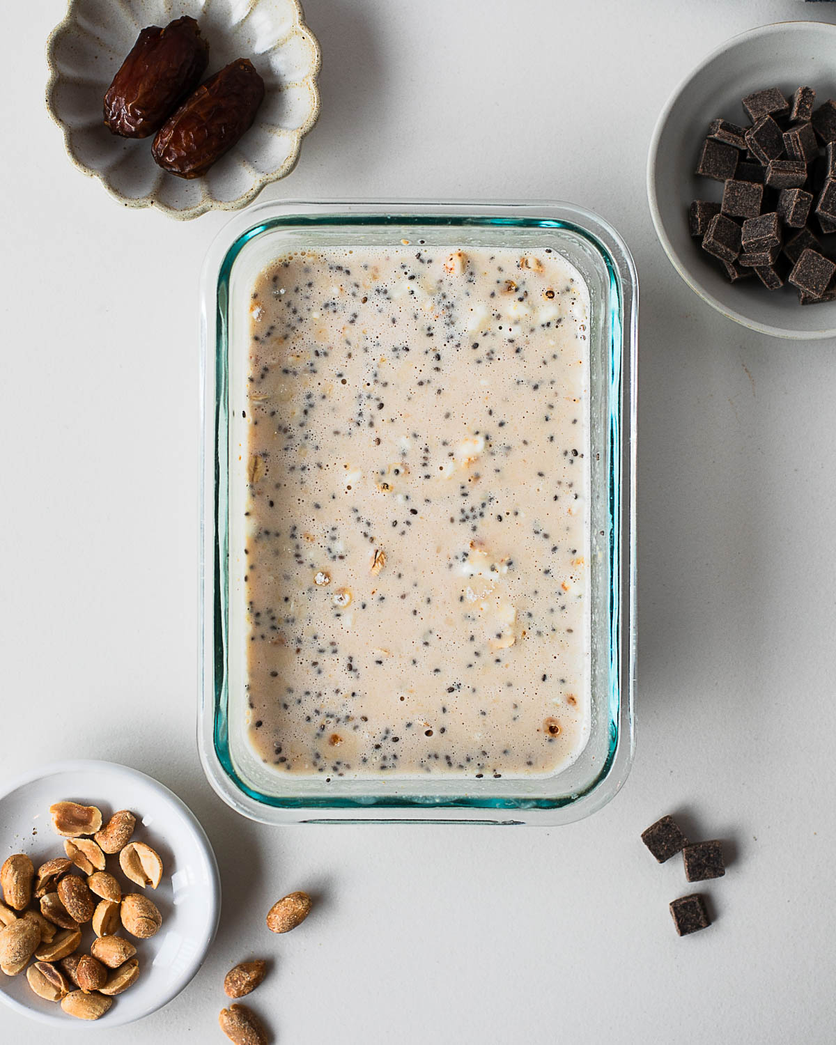 Snickers overnight oats mixture in a glass container with oats, chia seeds, almond milk, and dates before adding toppings