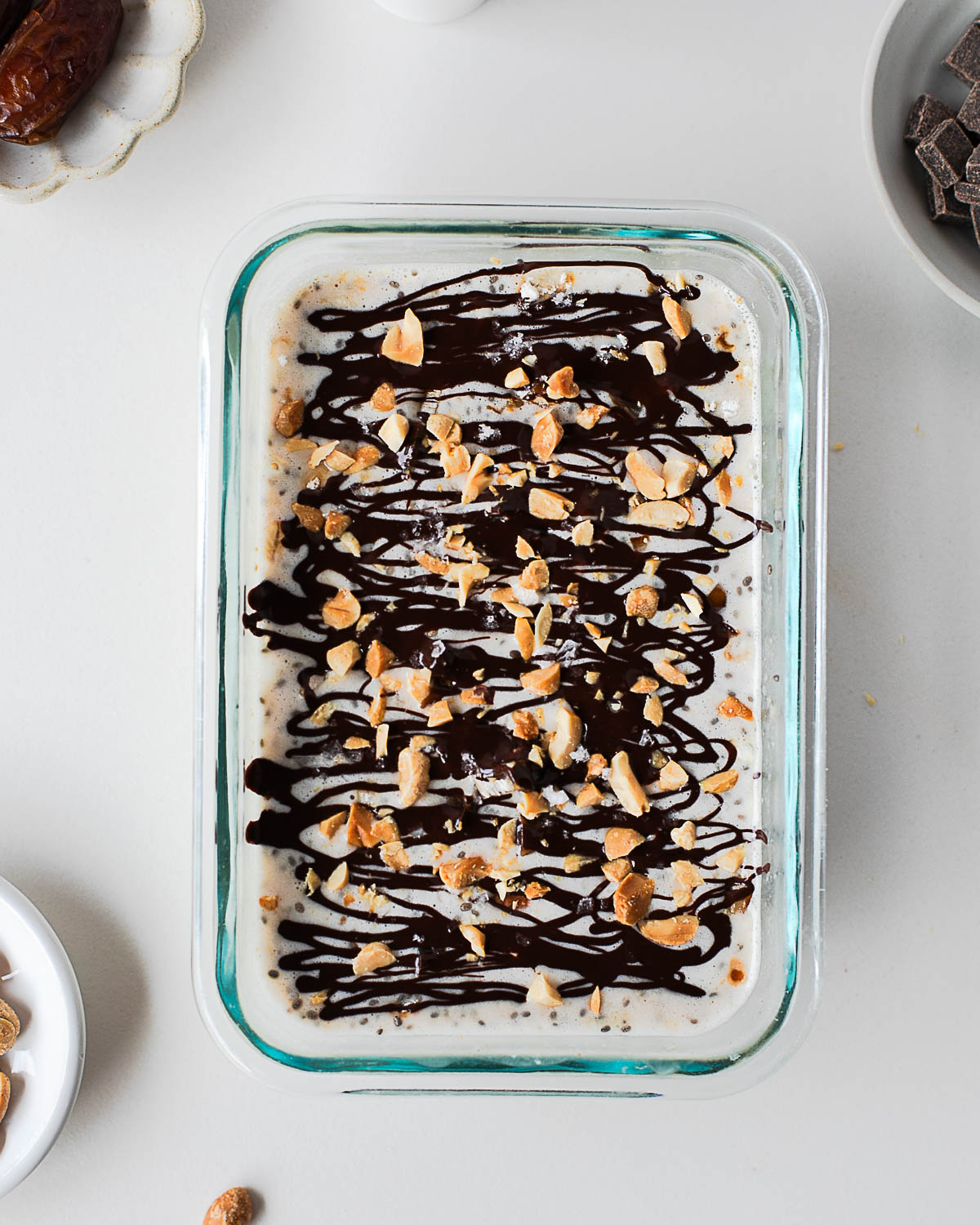 Snickers overnight oats topped with melted dark chocolate drizzle and chopped peanuts in a glass container