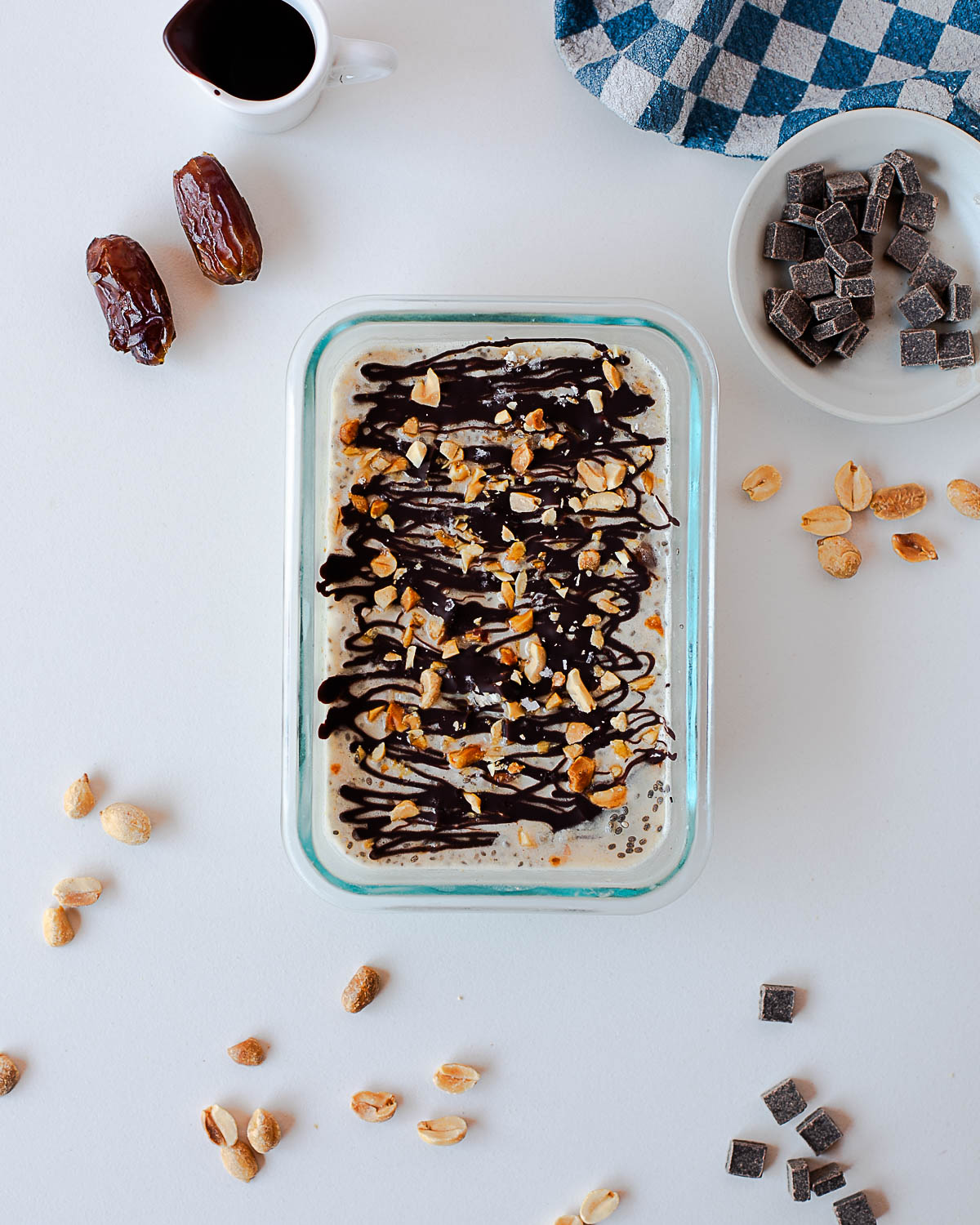 Snickers overnight oats with chocolate shell and peanuts, surrounded by dates, peanuts, and dark chocolate chips