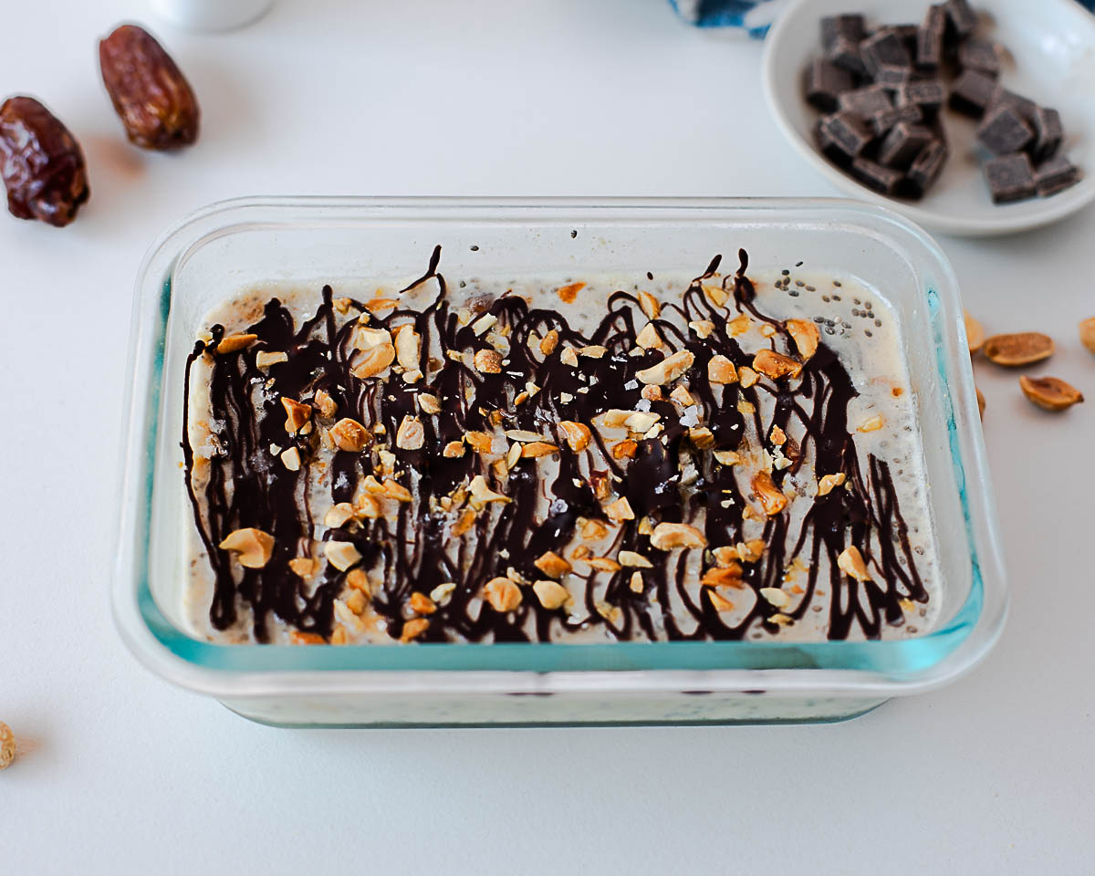 High-protein Snickers overnight oats in a glass meal prep container with chocolate and peanut topping