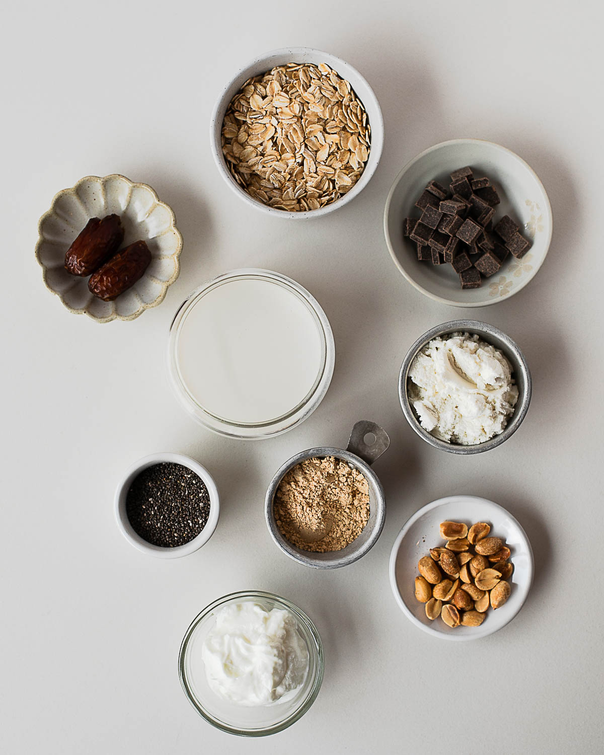 Ingredients for Snickers overnight oats including oats, dates, chia seeds, peanut butter powder, Greek yogurt, almond milk, peanuts, and dark chocolate