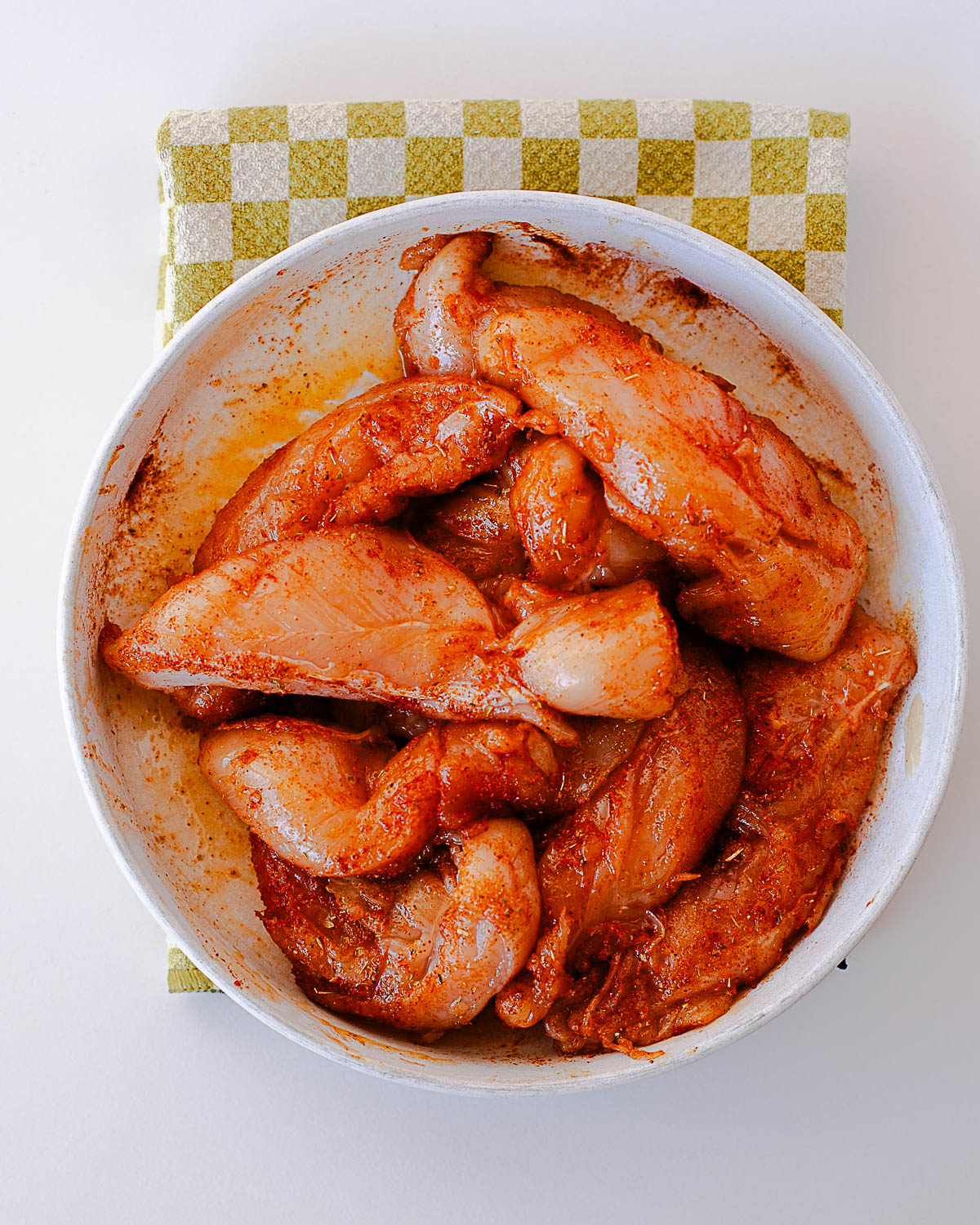 Seasoned raw chicken tenderloins in a white bowl with olive oil and spices, ready for the Traeger.