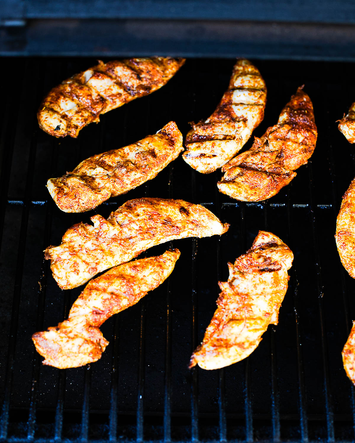 Chicken tenders grilling on a Traeger with smoky seasoning and char marks.