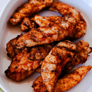 Cooked Traeger chicken tenders piled on a white serving dish with smoky spice rub.