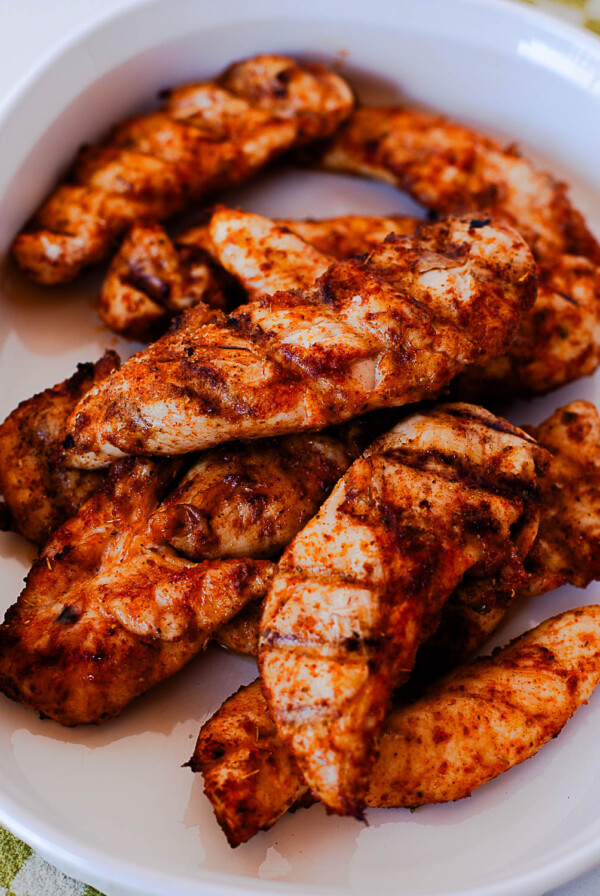 Cooked Traeger chicken tenders piled on a white serving dish with smoky spice rub.