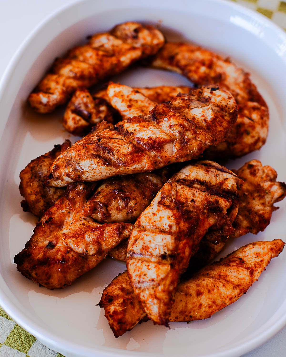 Cooked Traeger chicken tenders piled on a white serving dish with smoky spice rub.