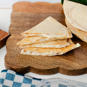 Stacked tuna melt quesadilla wedges on a wooden cutting board, lightly golden and crisp.