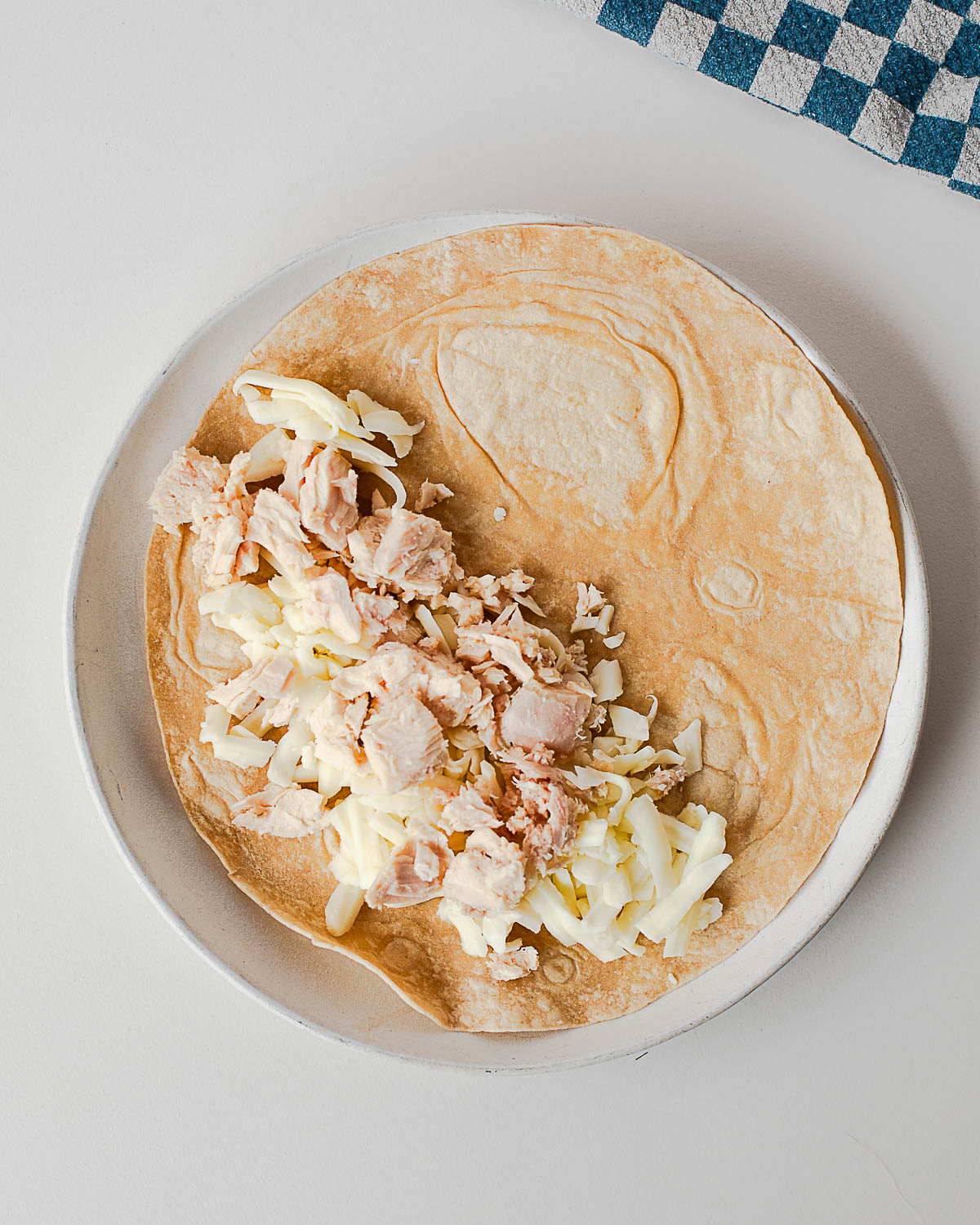 Overhead view of an open flour tortilla filled with shredded tuna and mozzarella cheese before folding into a quesadilla.